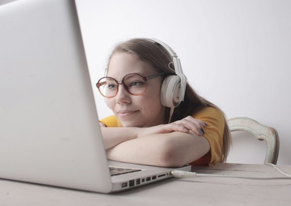Smiling woman wearing headphones and glasses, relaxing with a laptop indoors.