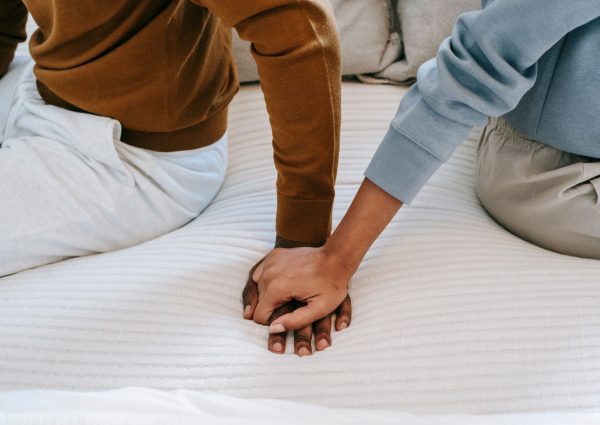 Crop faceless African American couple sitting on bed back to back and holding hands