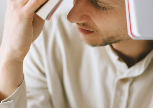 A man holds a book on his head, symbolizing stress and exhaustion in work life.